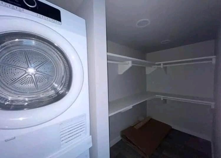Washer and closet space. On the left, a white front-loading dryer; to the right, an empty, white-walled closet with shelves and hangers.