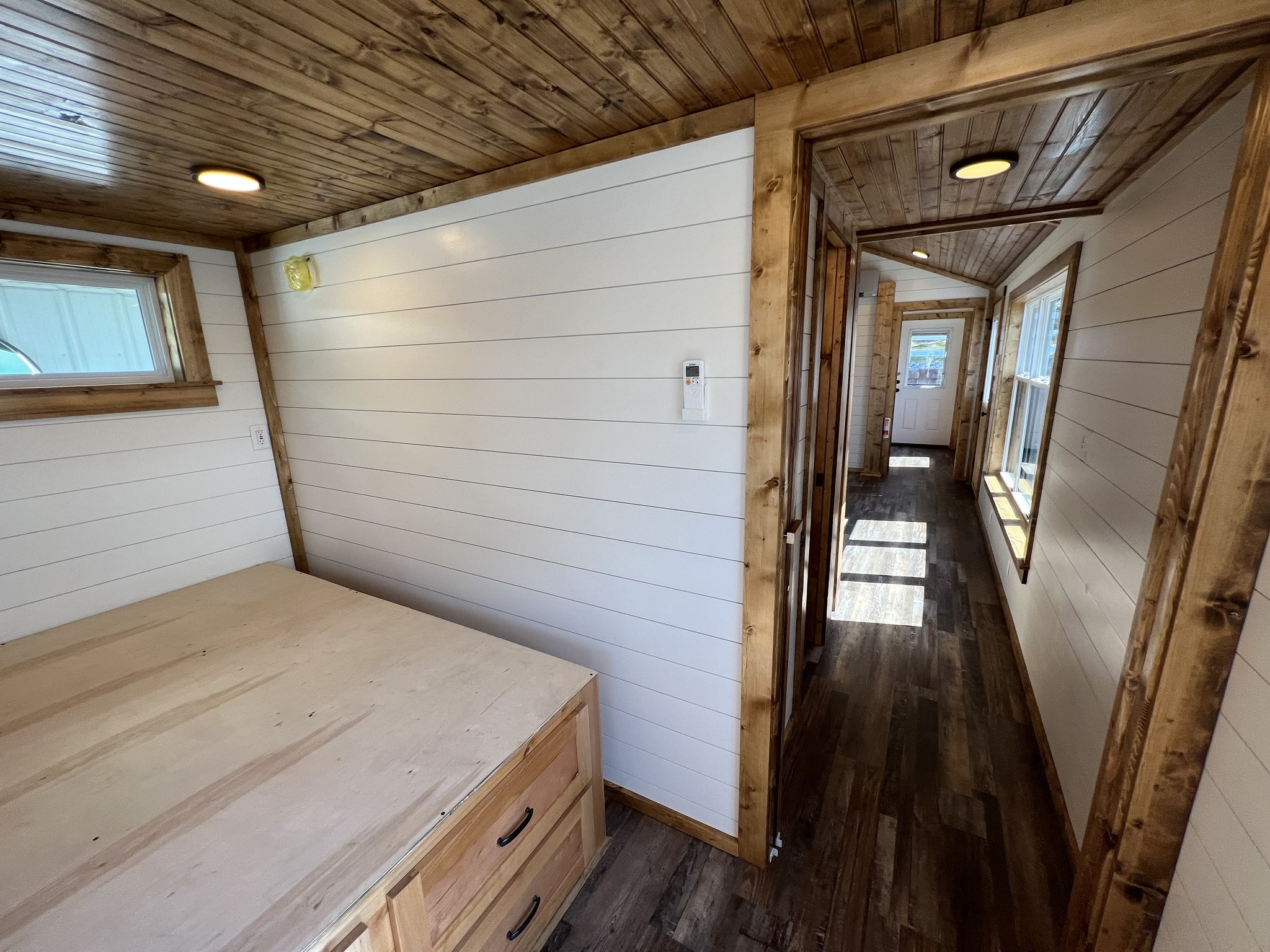 Wood-paneled tiny house interior with white shiplap walls and natural wood trim. Cozy hallway with warm lighting and rustic, earthy tones.