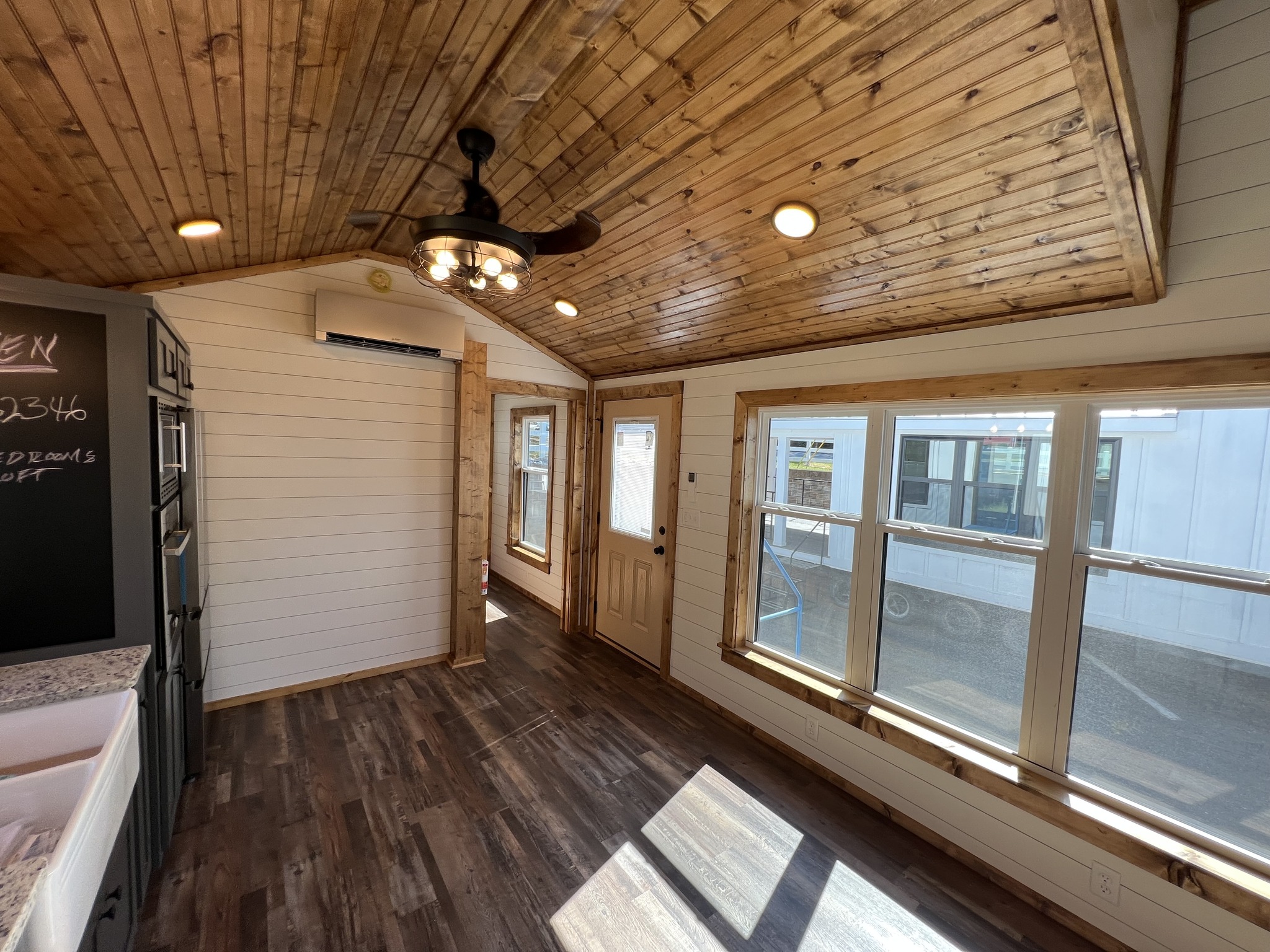 Cozy wooden interior with a sloped ceiling and recessed lighting. Large windows and a ceiling fan create a warm, inviting atmosphere.