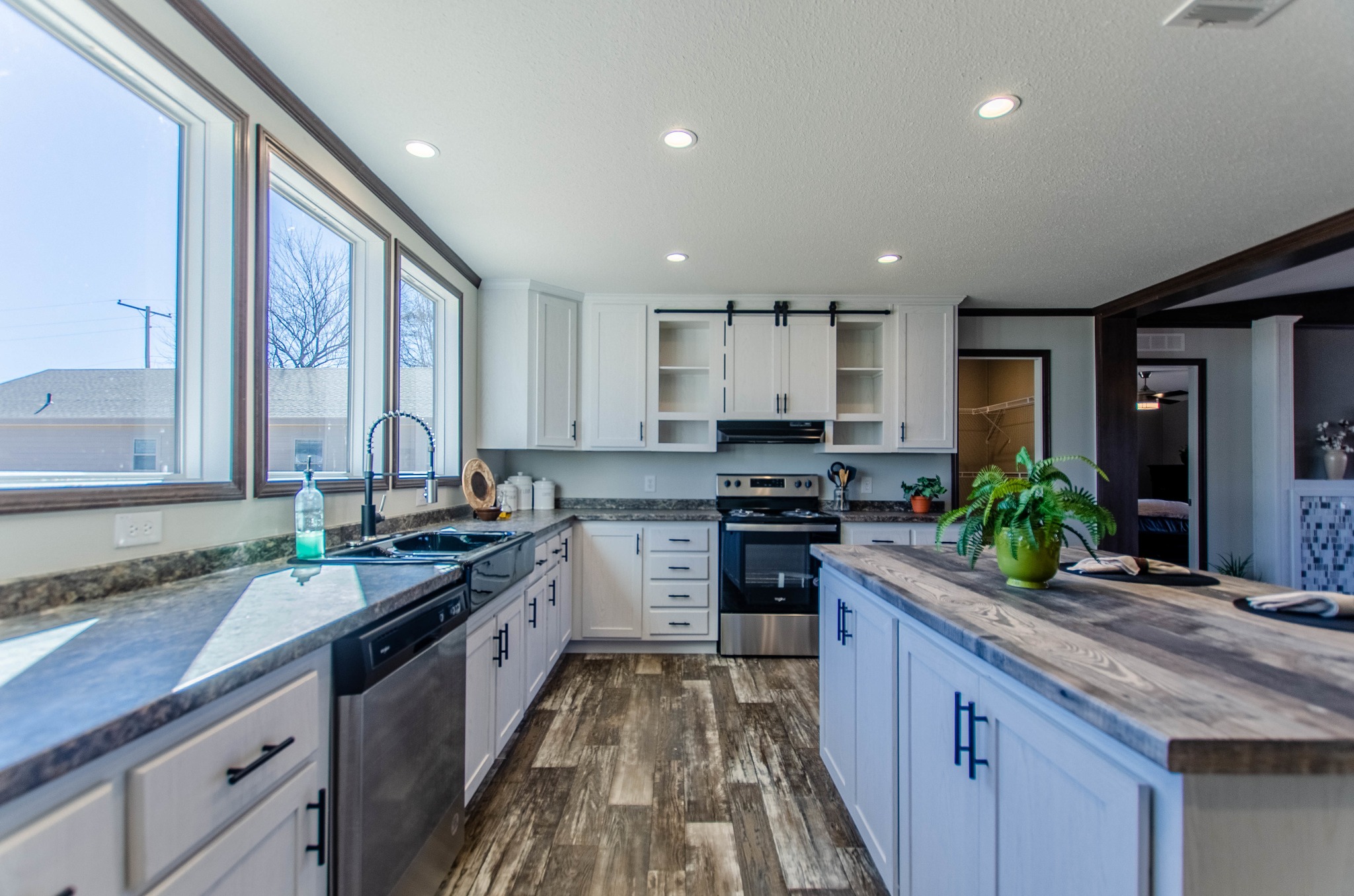 Bright kitchen with white cabinets, black appliances, and a wooden island. Large windows illuminate the room, creating a welcoming atmosphere.