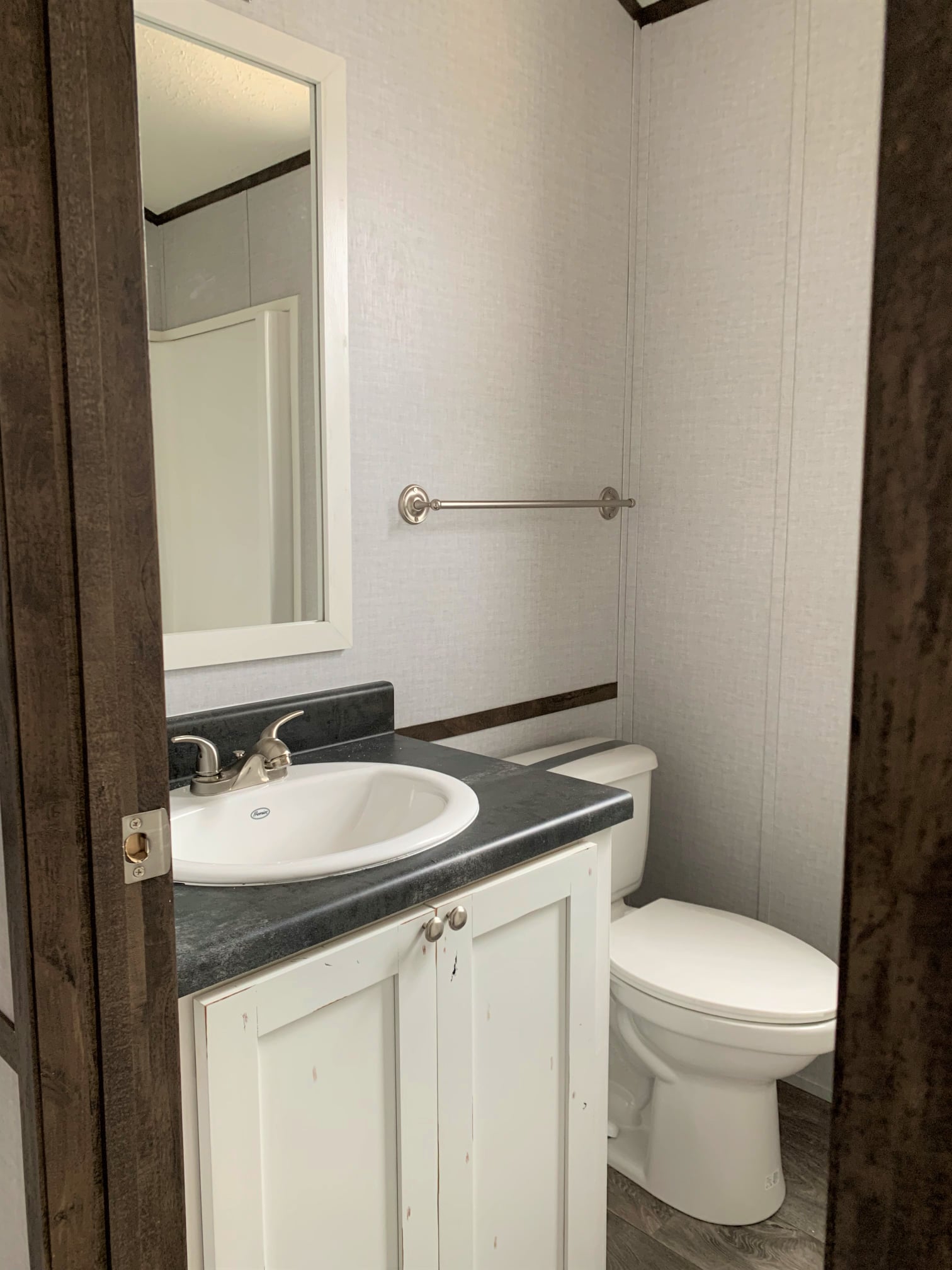 Small bathroom with a white sink and cabinet on the left, a wall-mounted mirror, and a toilet on the right. Neutral tones create a simple, clean look.