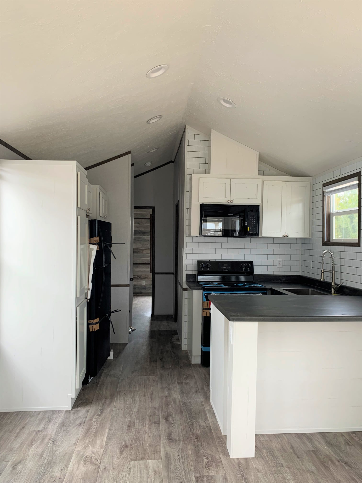 Modern kitchen with white cabinets, black countertops, and stainless appliances. Notable features include a subway tile backsplash and wood flooring.