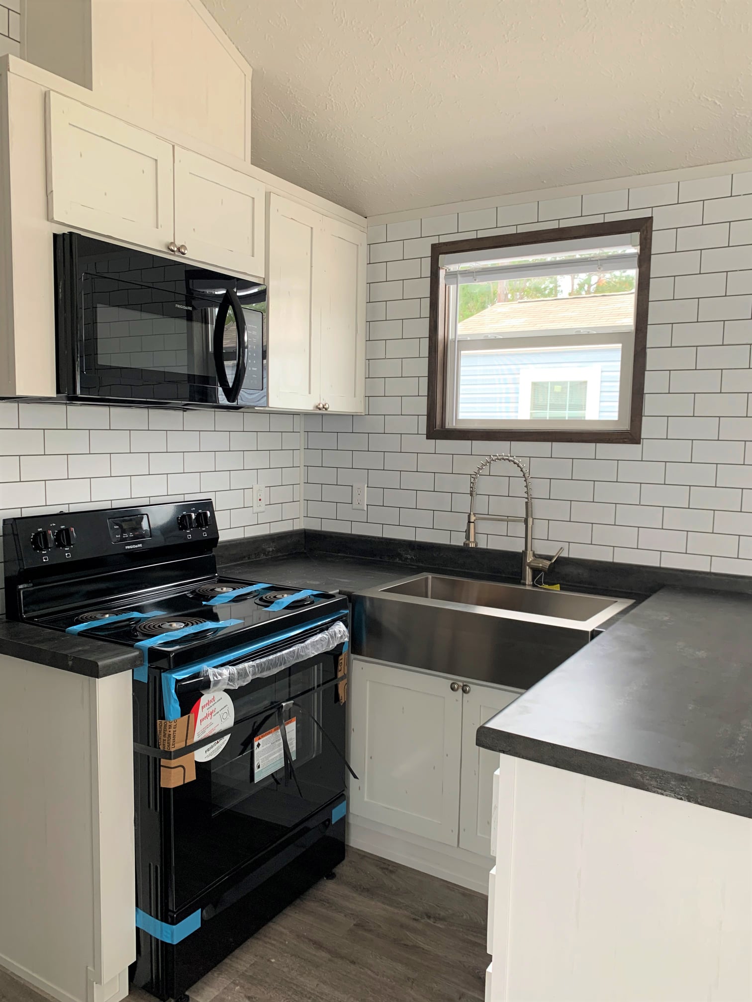 Compact kitchen with white cabinets, black appliances, and stainless steel sink. Subway tile backsplash and a window add brightness. Modern, clean design.