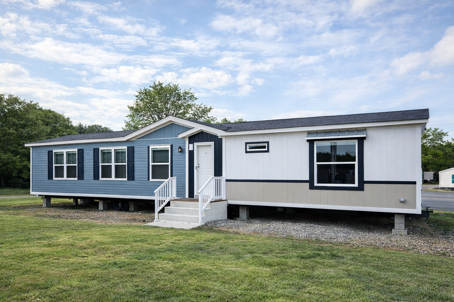 A modern blue and white mobile home on a grassy lot, featuring large windows and a small front porch under a partly cloudy sky, conveying tranquility.