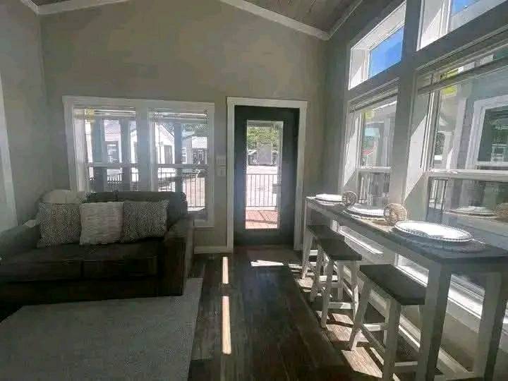 Bright living room with large windows, a cozy gray sofa with cushions, and a tall dining table with stools, creating a warm and inviting atmosphere.