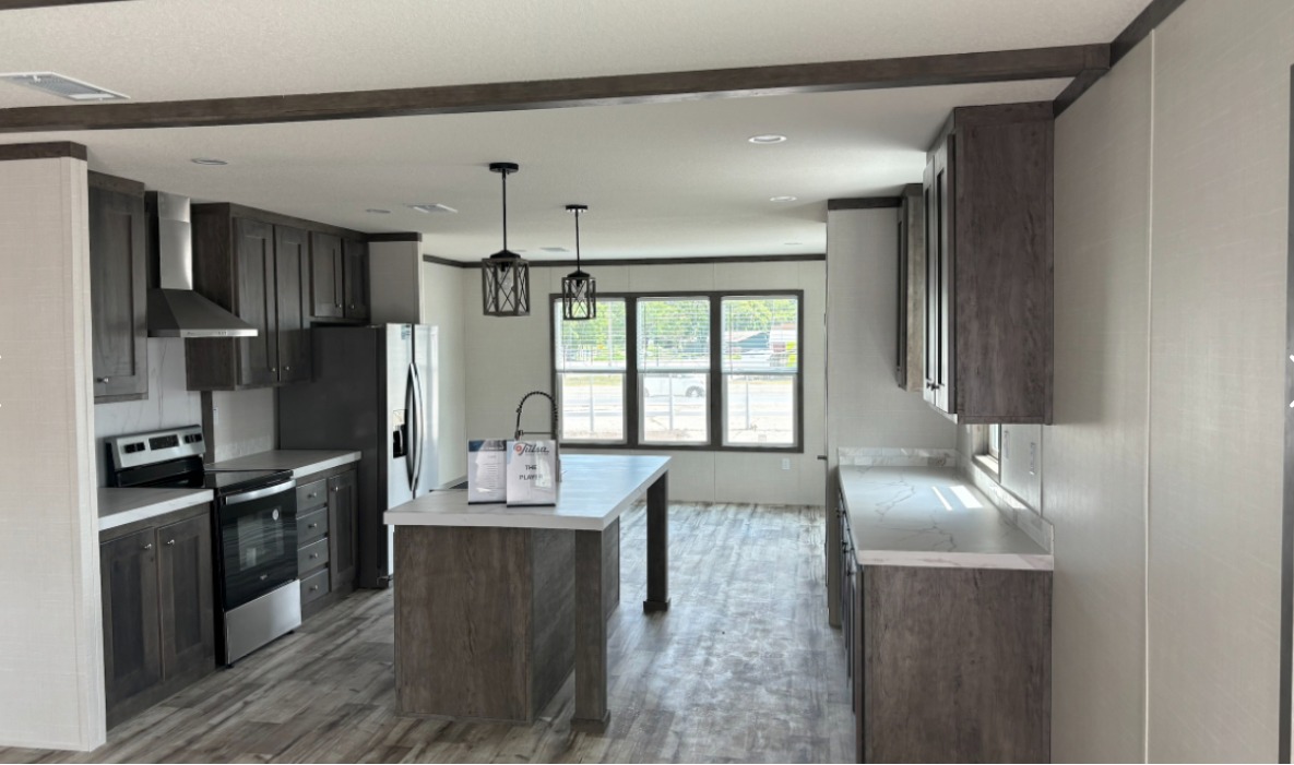 Modern kitchen with dark wood cabinets, an island, and stainless steel appliances. Large windows illuminate the space with natural light.