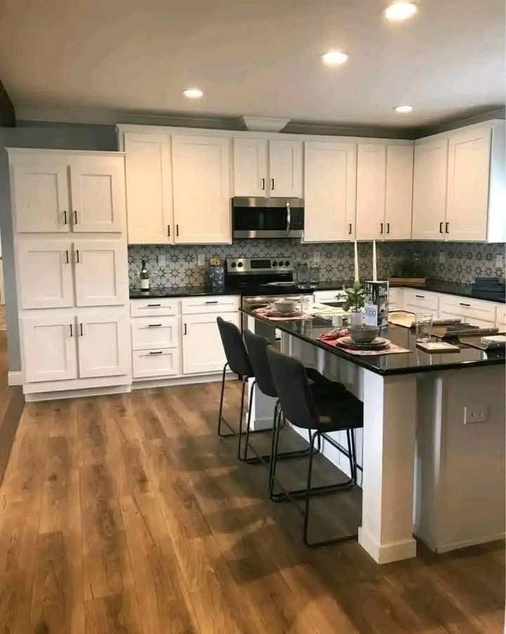 Modern kitchen with white cabinets, patterned backsplash, and wooden flooring. A dark island has stools and table settings, creating a cozy, inviting atmosphere.