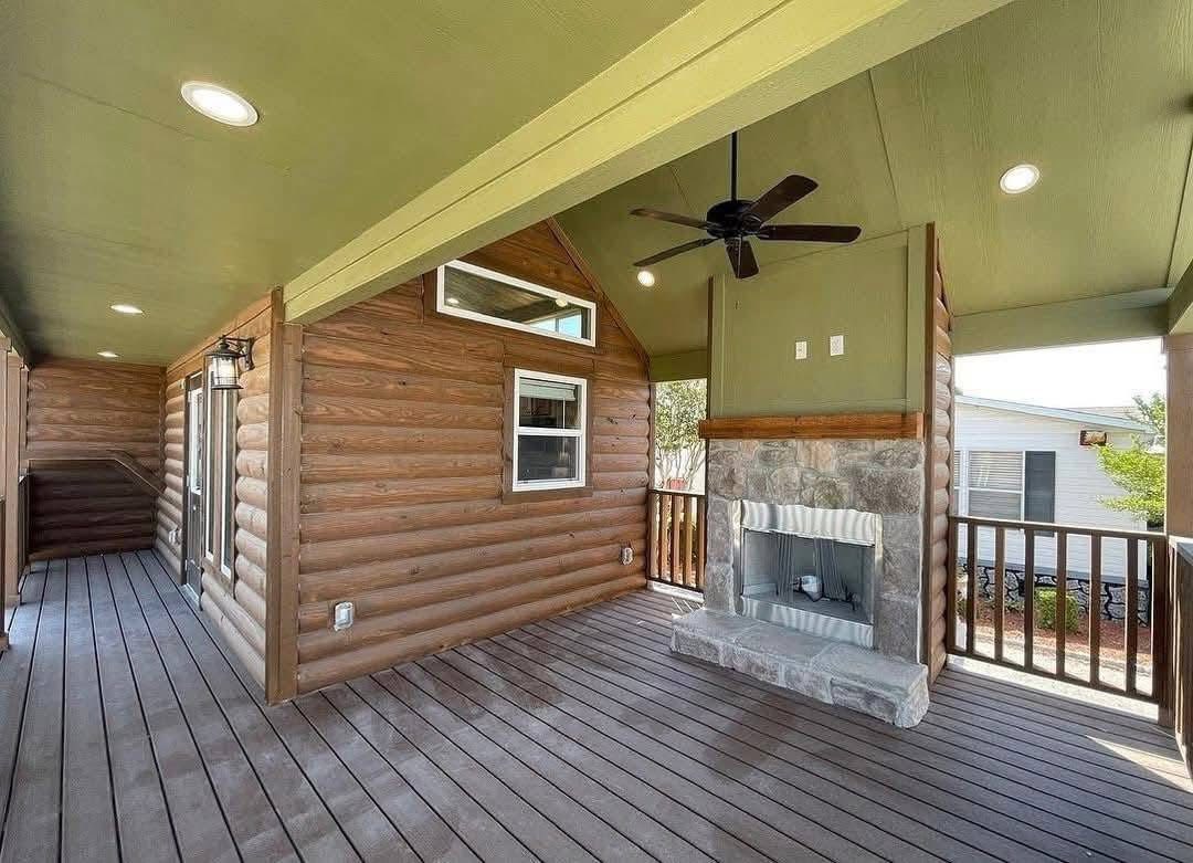 Covered porch with wooden walls and ceiling features recessed lighting and a ceiling fan. A stone fireplace adds a cozy touch. The area feels inviting and warm.