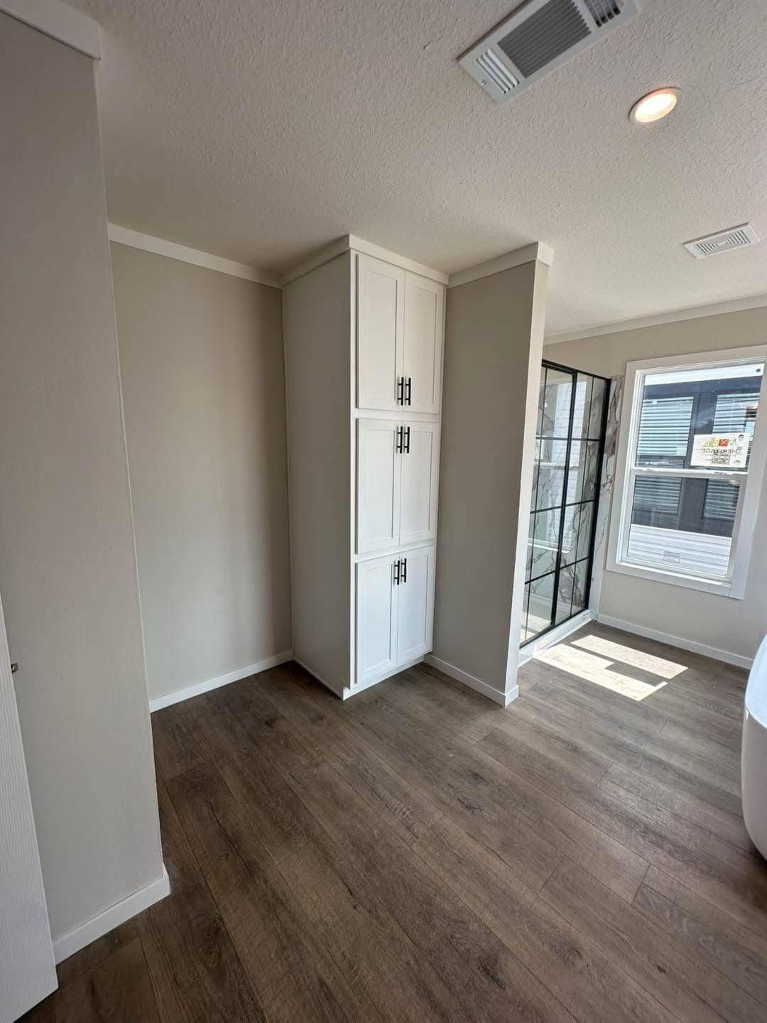 A room with wood flooring, white built-in cabinets, and a large window letting in natural light. The atmosphere is bright and modern.