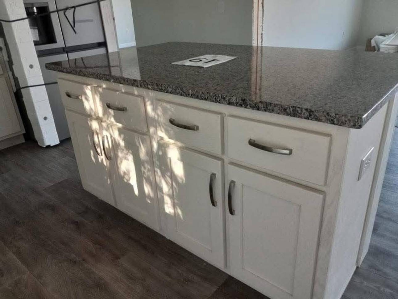 Kitchen with white island cabinets and dark granite countertop, wooden floor, shadow of leaves on cabinets, creating a calm, natural ambiance.