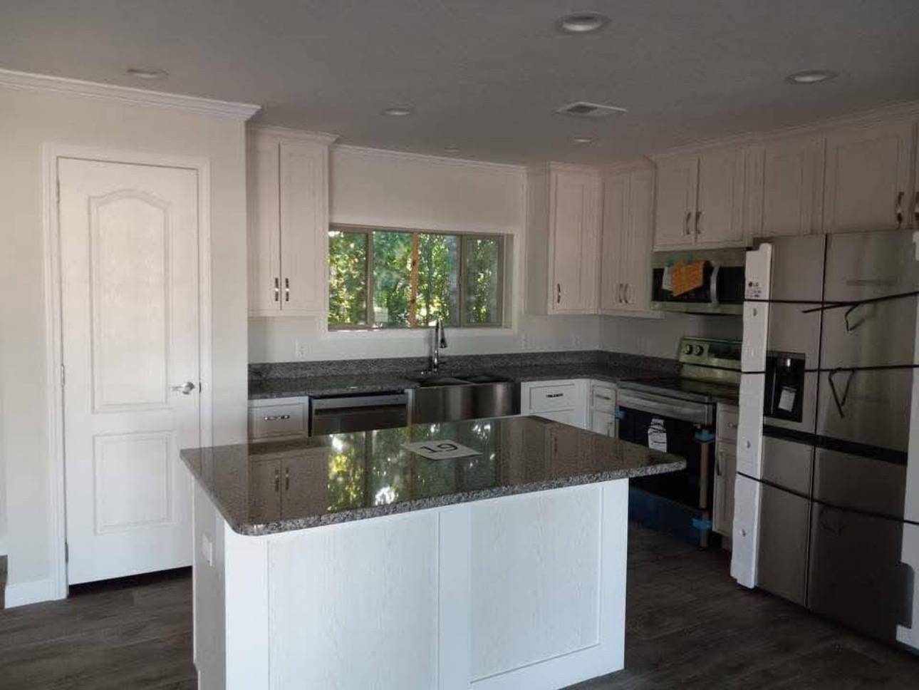 Modern kitchen with white cabinets, stainless steel appliances, and a granite island. A window above the sink lets in natural light, creating a sleek, bright atmosphere.