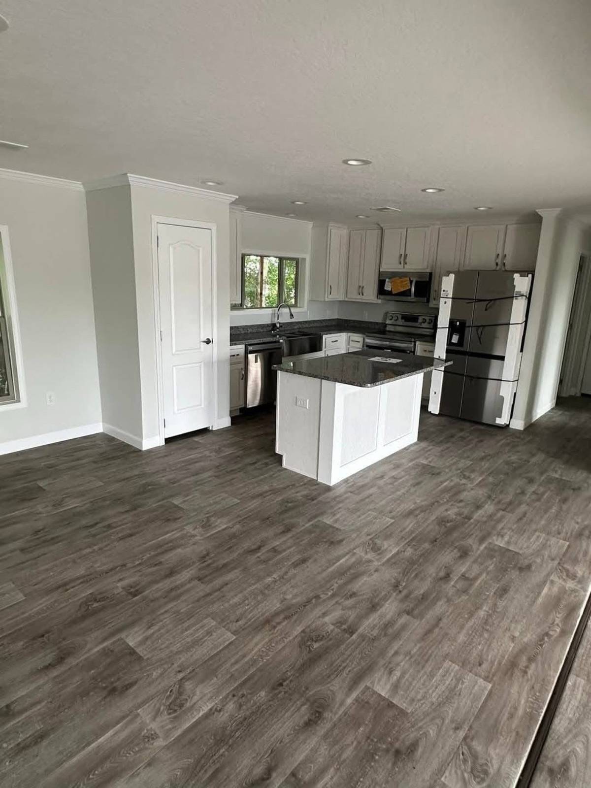 Modern kitchen with gray wood flooring, white cabinets, and stainless steel appliances. Central island features a granite countertop.