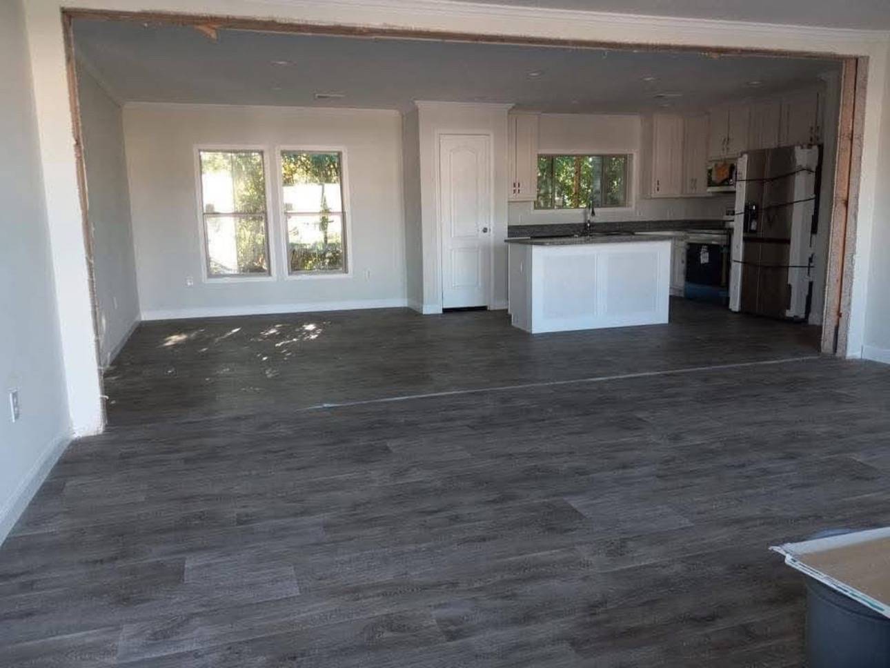 Spacious, open-plan interior with dark hardwood floors, white walls, and a modern kitchen featuring a large central island and stainless steel appliances.