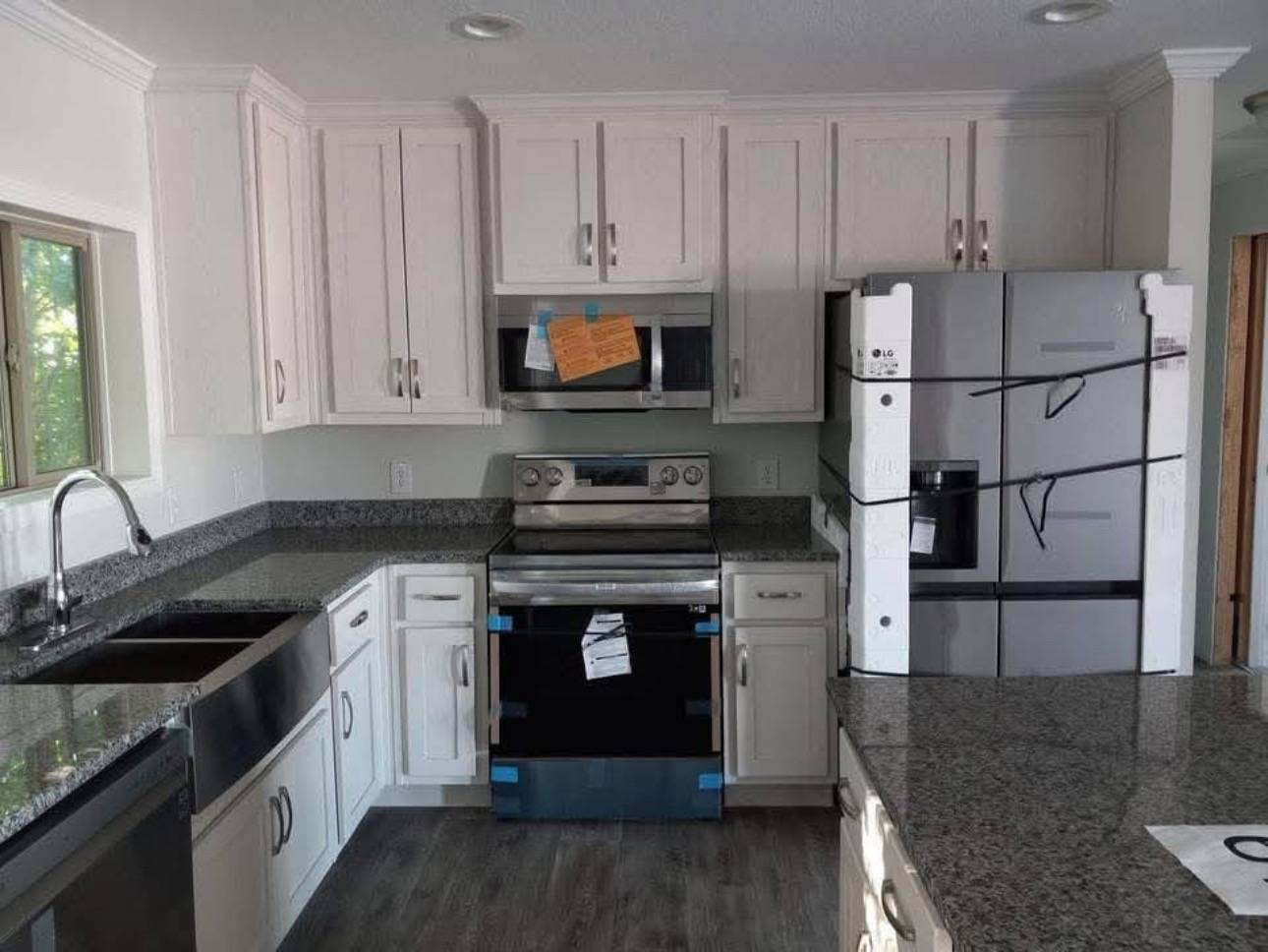Modern kitchen with white cabinets, stainless steel appliances, and granite countertops. New stove and fridge have packaging materials. Bright and clean.