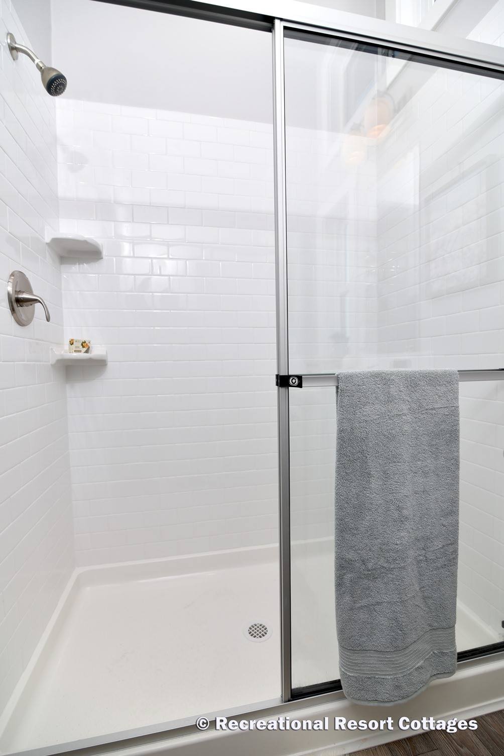 Modern shower with white subway tiles, silver fixtures, and glass sliding doors. A gray towel hangs on the door, creating a clean and simple ambiance.