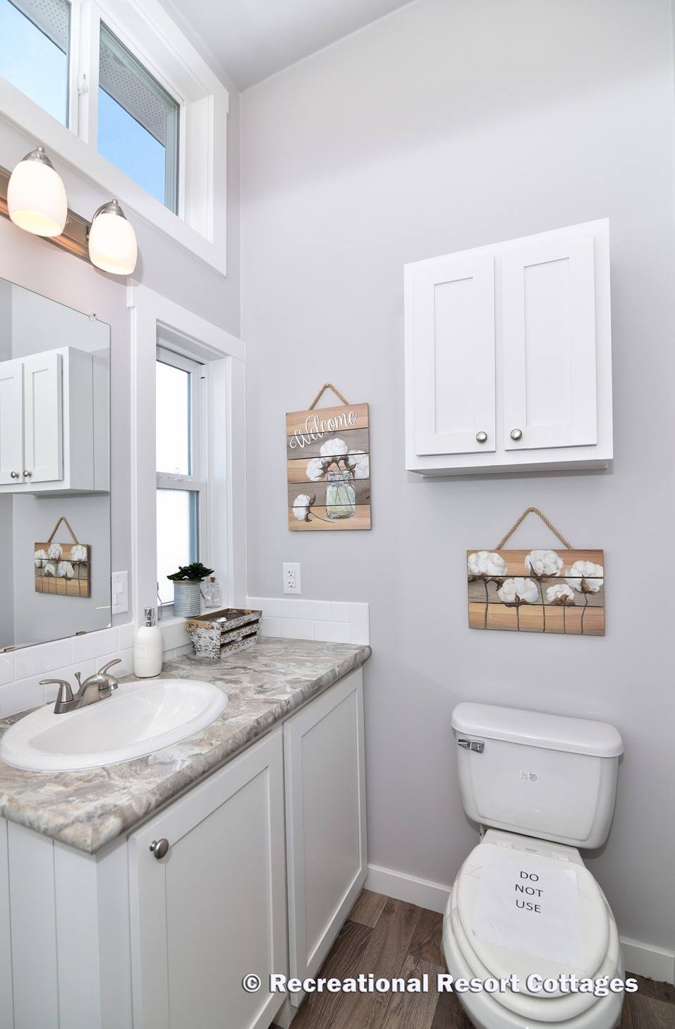 Modern bathroom with marble countertop, white vanity, and decorative signs. Bright lighting and a small plant add a fresh, welcoming feel.