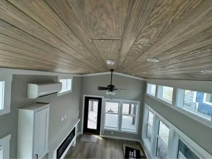 Spacious room with wood-paneled ceiling, large windows, a ceiling fan, and light wood flooring. Modern decor with a cozy, airy feel.