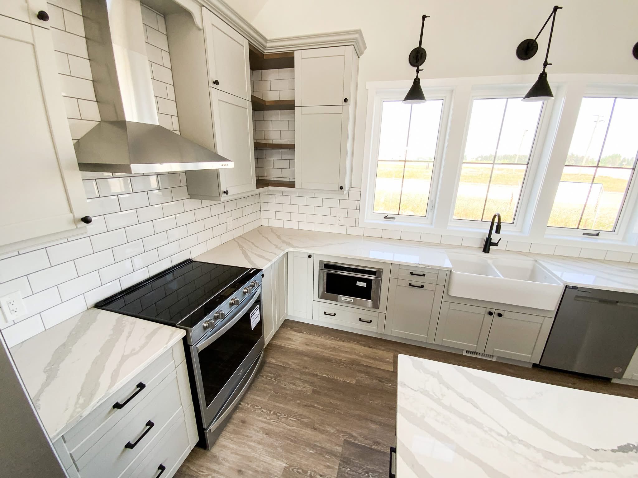 Modern kitchen with white cabinets, subway tile backsplash, stainless steel appliances, and black fixtures. Large windows provide natural light.
