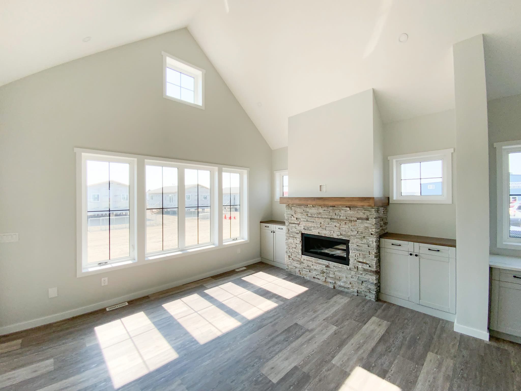 Bright, spacious living room with vaulted ceiling, large windows, and a stone fireplace. Modern, airy ambiance with light wood floors.