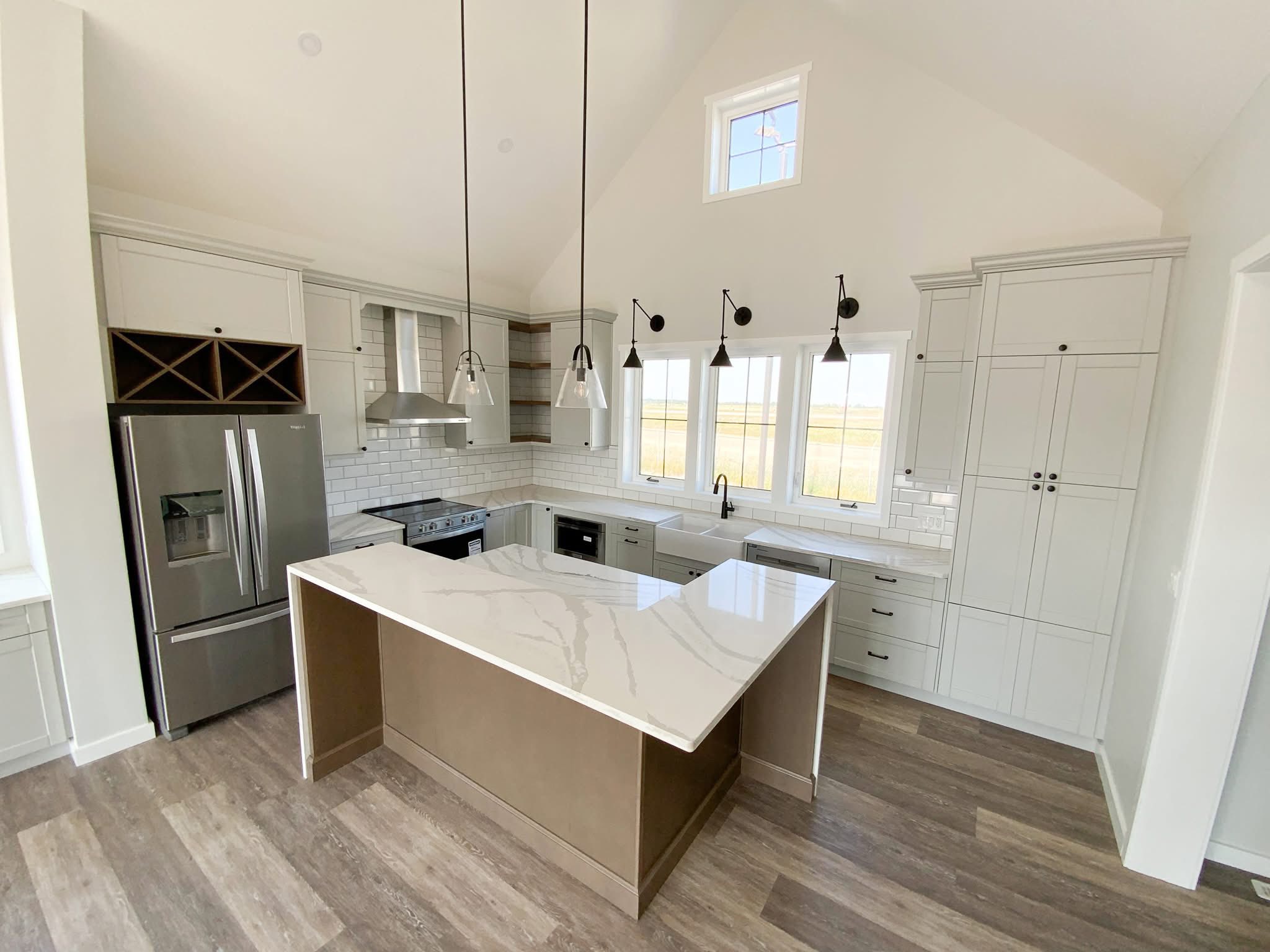 Bright, modern kitchen with high ceilings, a sleek marble island, stainless steel appliances, pendant lights, and white cabinetry, exuding elegance.