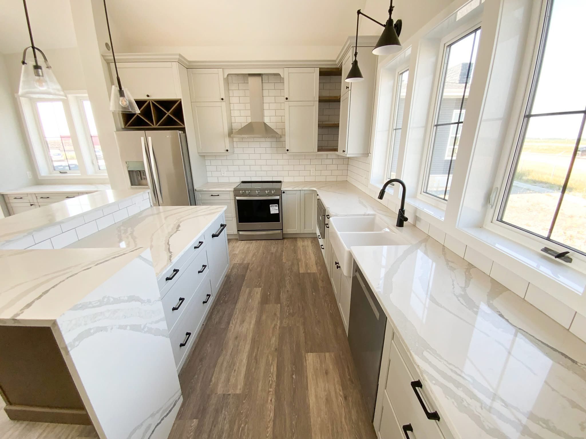 Modern kitchen with white cabinetry, marble countertops, and stainless steel appliances. Large windows brighten the space, creating an airy and welcoming atmosphere.