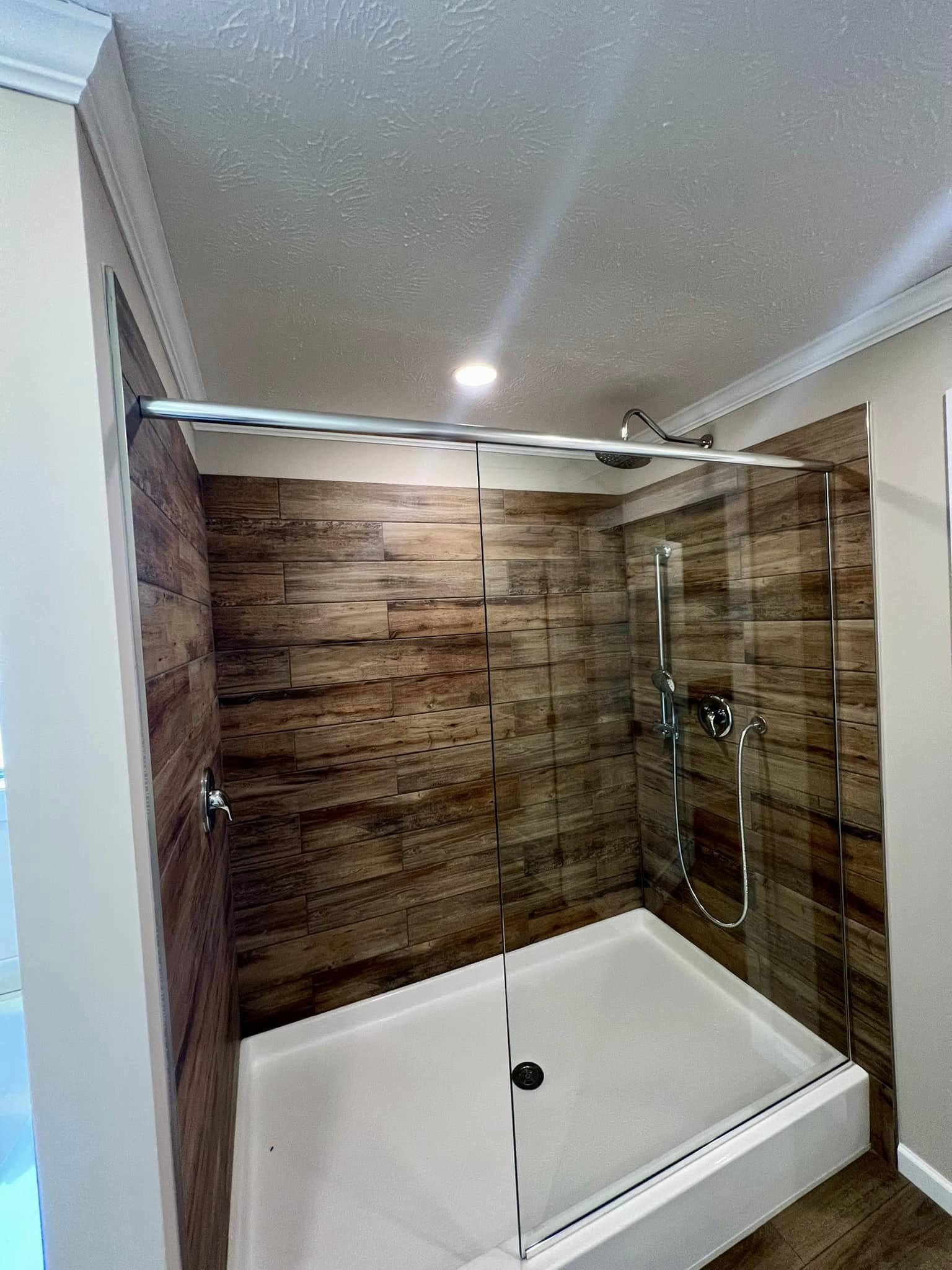 Modern shower with glass doors and wood-textured tile walls, illuminated by a ceiling light. The space feels clean and sleek.