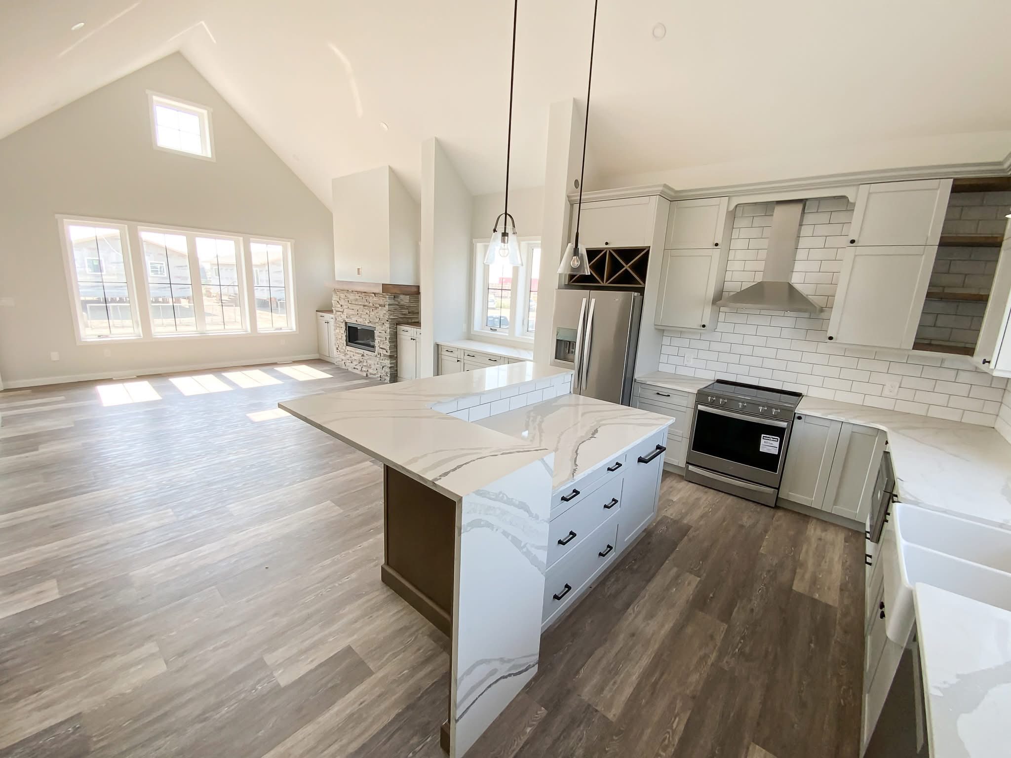 Spacious kitchen and living area with high vaulted ceilings, light wood flooring, and a large island. Sunlit windows and modern appliances enhance the bright, airy feel.