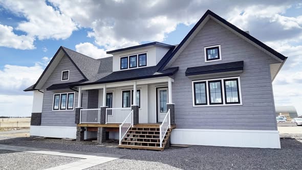 Modern gray house with white trim, gabled roof, and a front porch with stairs. Set against a cloudy sky, creating a calm suburban atmosphere.