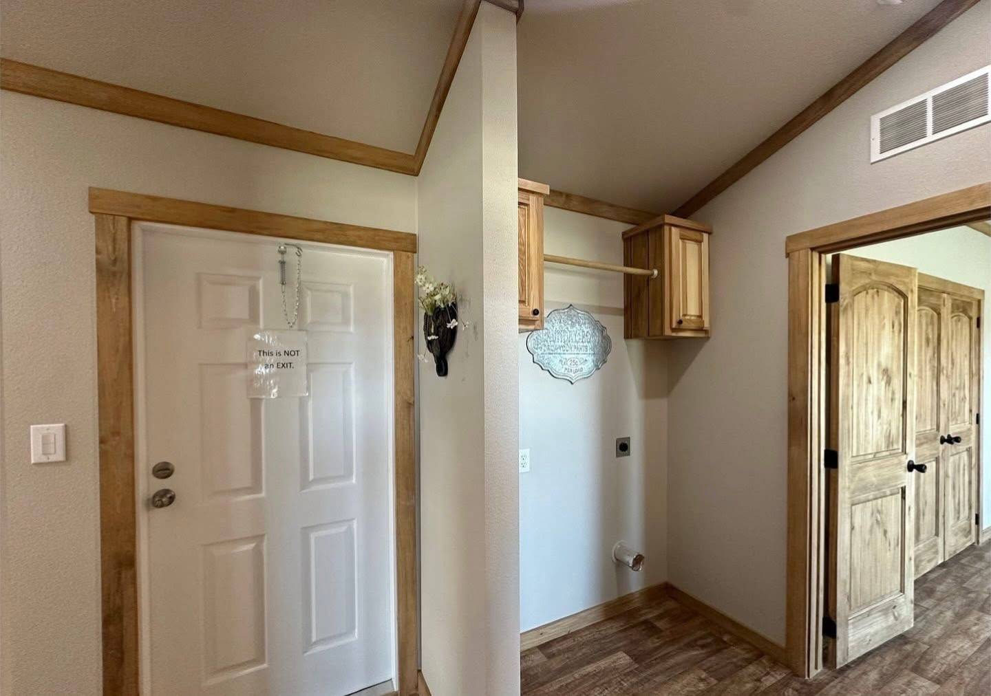 A cozy hallway features a white door labeled "This is NOT an exit," light wood trim, a small mounted shelf, and an open closet area with wooden cabinets.