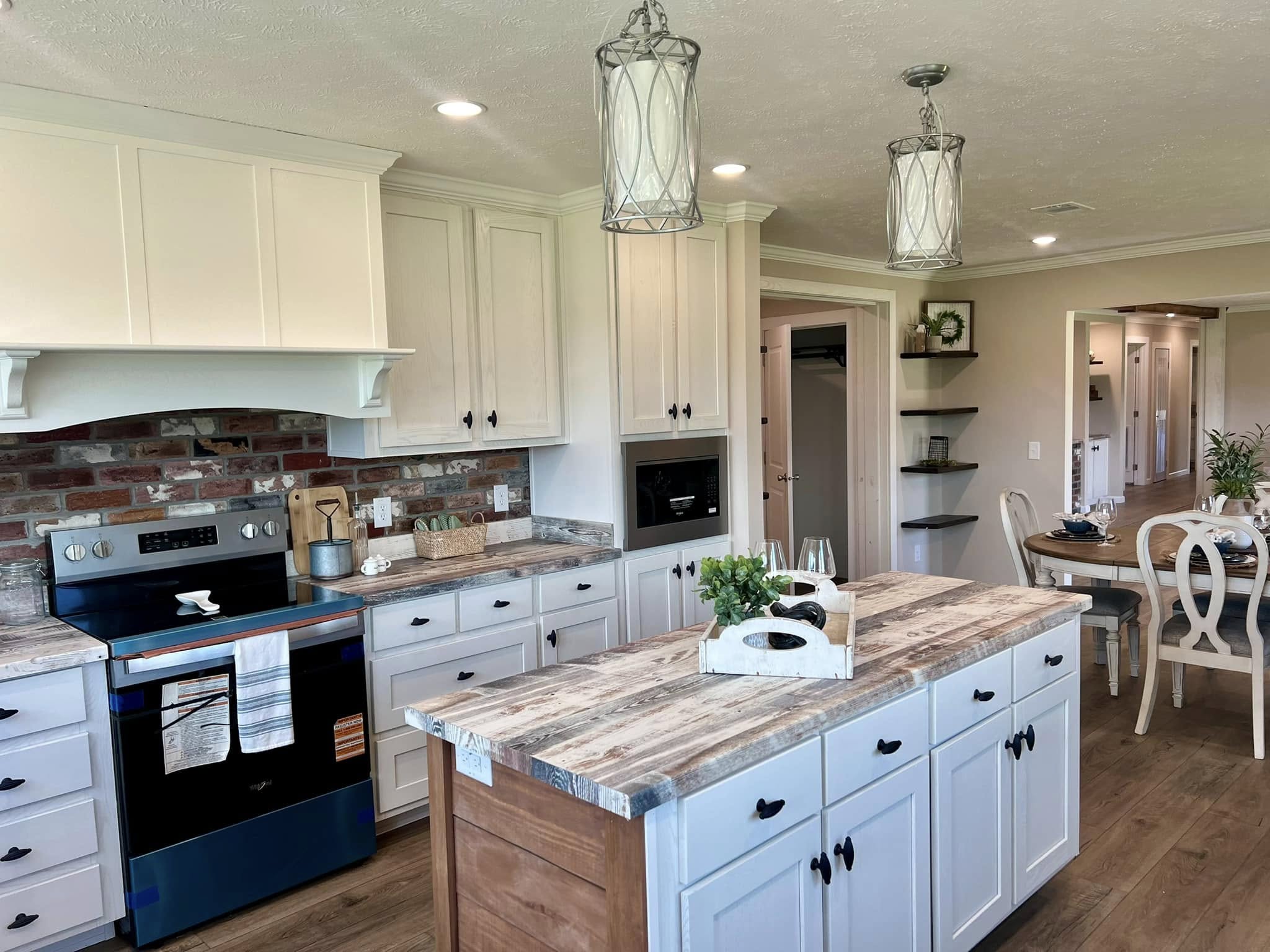 Spacious kitchen with rustic charm, featuring white cabinets, a wooden island, brick backsplash, modern stove, and elegant lighting fixtures. Cozy dining area visible.