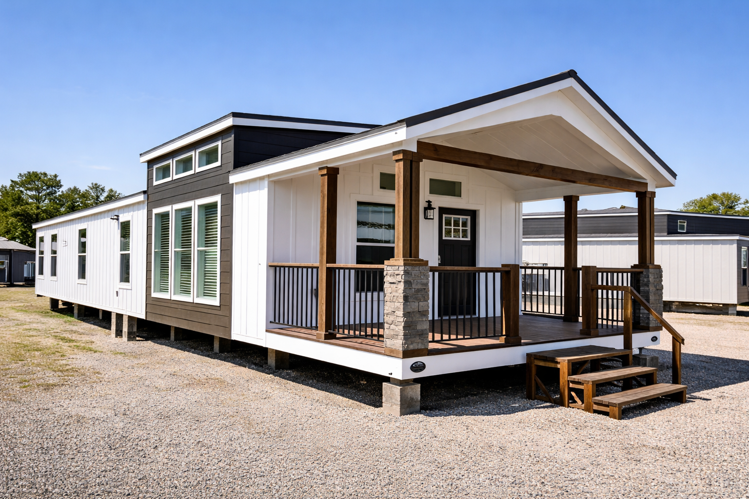 Modern manufactured home with a black and white exterior, large windows, and a wooden porch with steps. The sky is clear and blue, conveying a sense of calm.