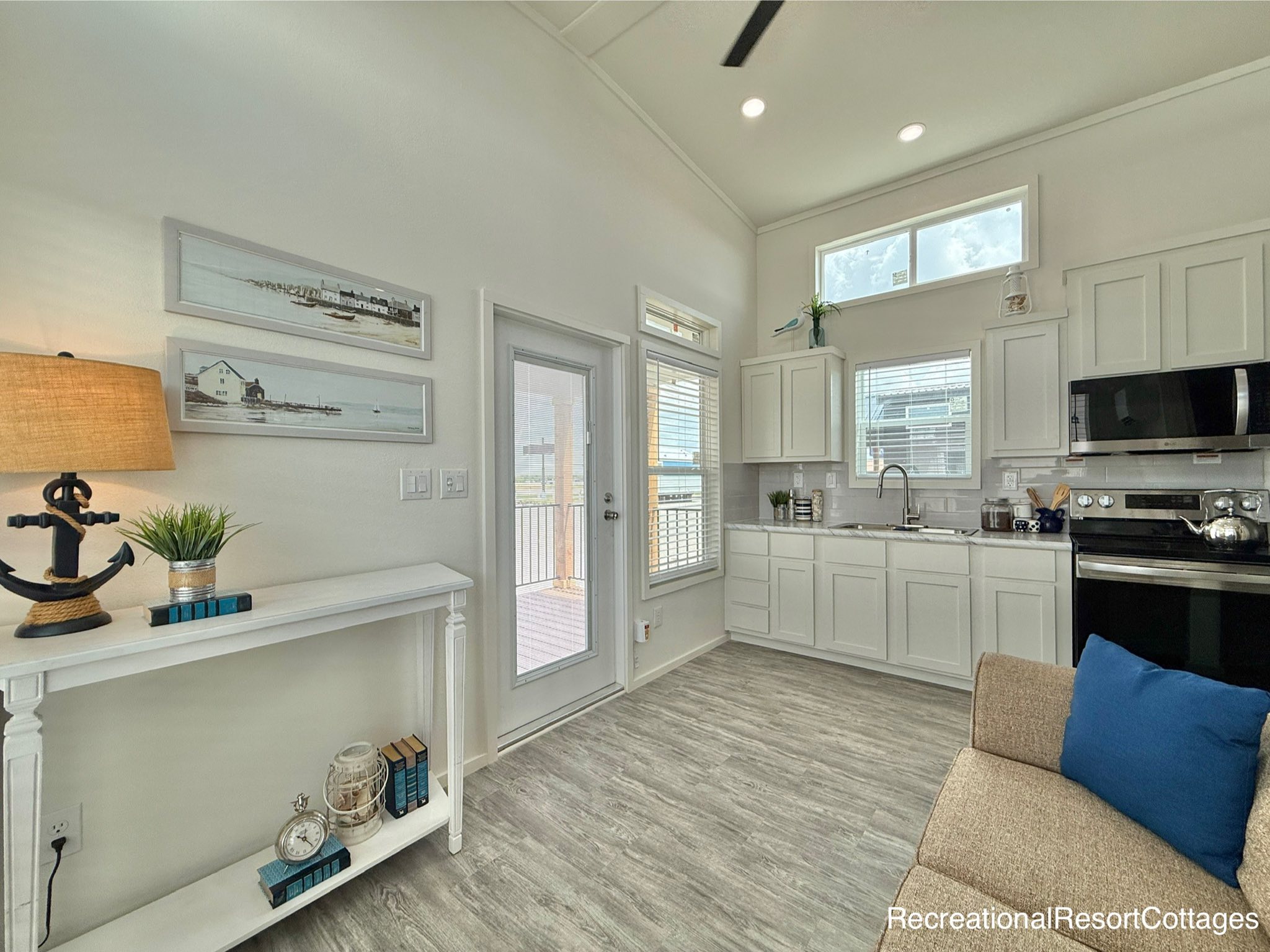 Bright, cozy kitchen and living area with white cabinets, modern appliances, a small couch with blue cushions, and nautical-themed decor.