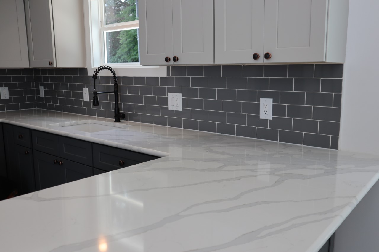 Modern kitchen with white marble countertops, dark gray lower cabinets, and light gray upper cabinets. The backsplash features dark gray subway tiles.