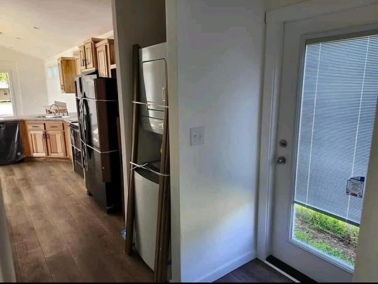 Narrow kitchen with wooden cabinets and black appliances. Stack washer-dryer against a white wall near a door with blinds. Bright, homey atmosphere.