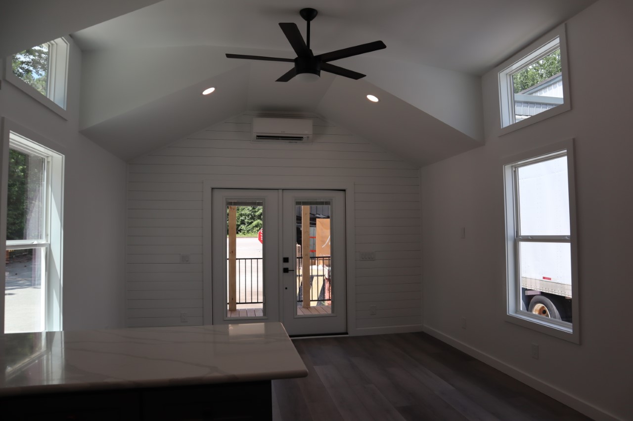 Modern, minimalist room with vaulted ceiling, large windows, and a ceiling fan. Glass double doors lead outside, creating an airy, open feel.