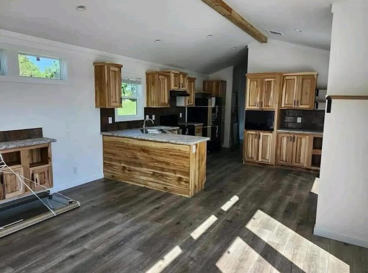 Spacious kitchen with natural light, featuring wooden cabinets, a central island with a sink, and modern appliances on wood flooring. Warm and inviting.
