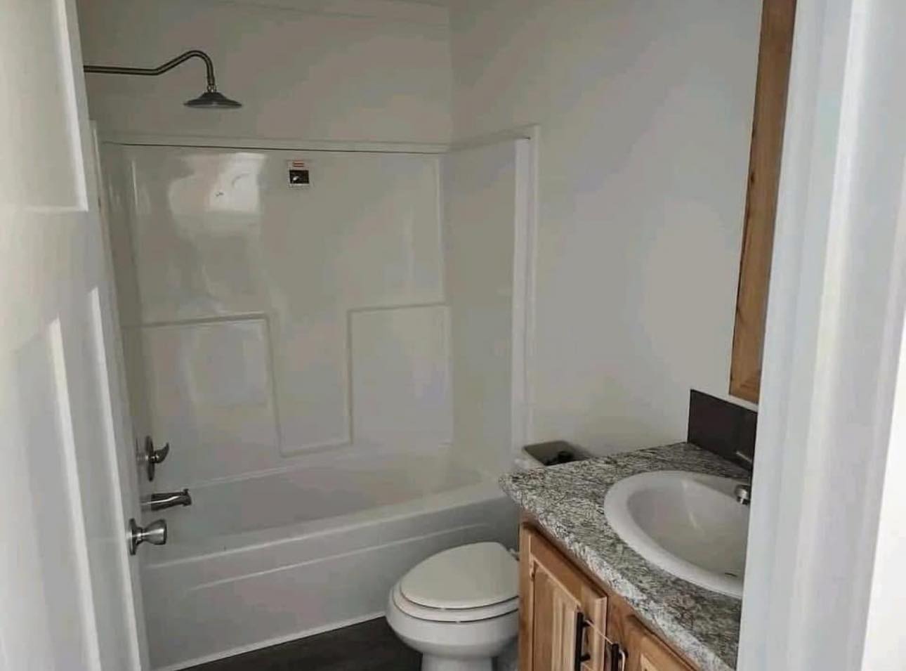 Narrow bathroom with a showerhead above a bathtub, and a toilet partially blocking access. A granite countertop sink is on the right.