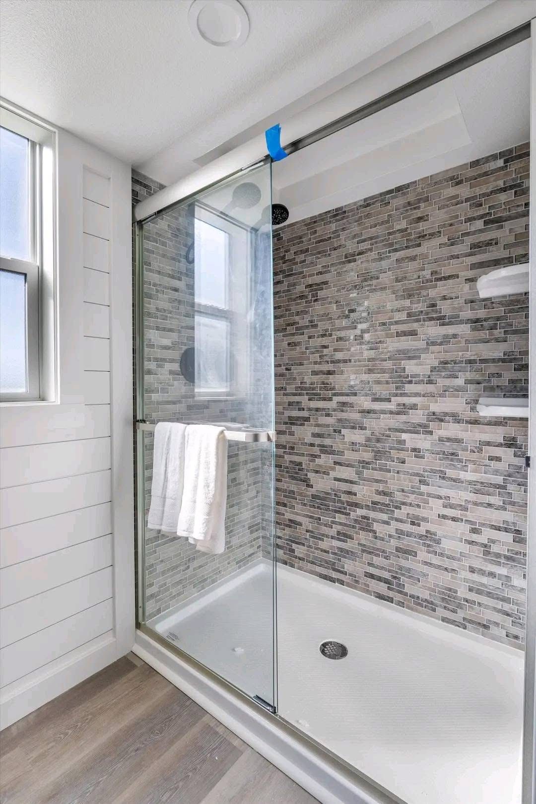 Modern bathroom with a tiled walk-in shower featuring gray stone-patterned walls, a sliding glass door, and a white towel hanging on the handle.