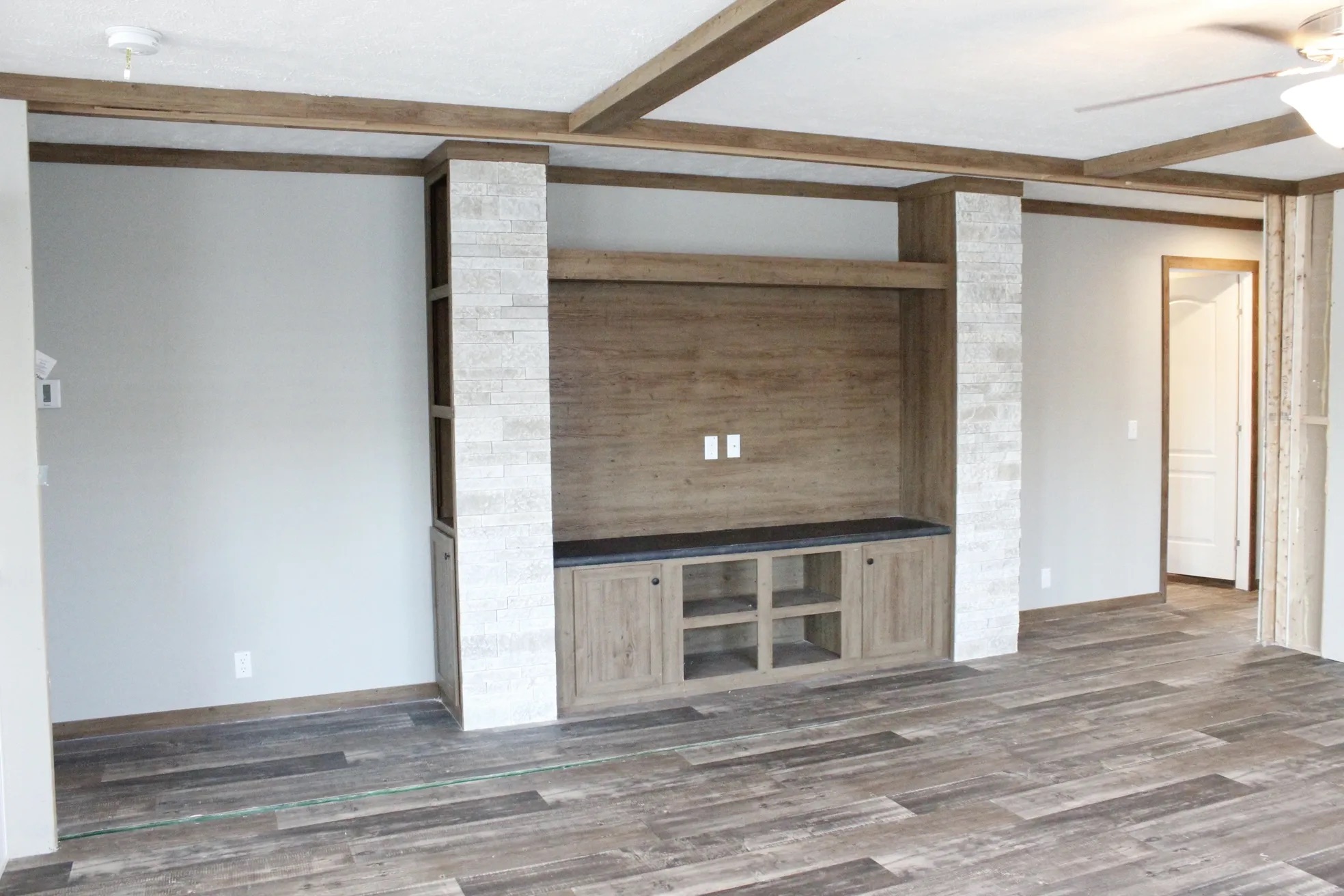 Modern living room with wood-style floor, built-in shelving, and neutral walls. Ceiling fan and recessed lighting create a warm, inviting tone.