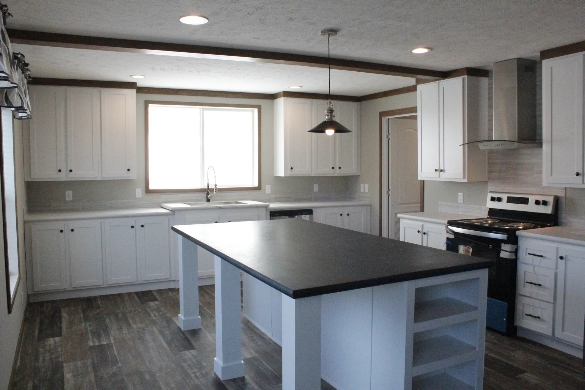 A spacious, modern kitchen with white cabinets, a black countertop island, stainless steel appliances, and wood-style flooring, evoking a clean, contemporary feel.