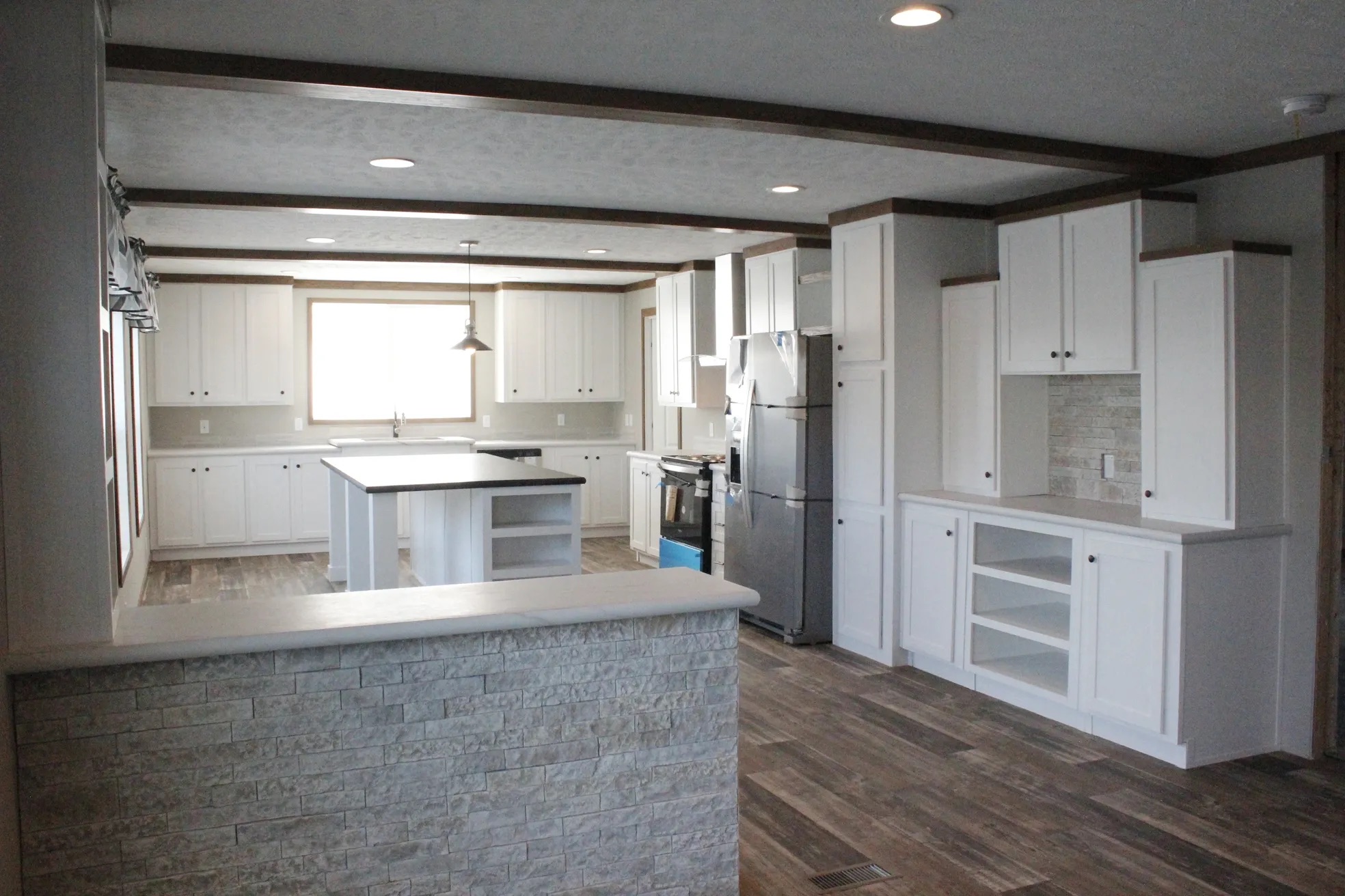 Spacious kitchen with white cabinets, stainless steel appliances, and a central island. Stone accent wall and wood-look flooring add a cozy touch.