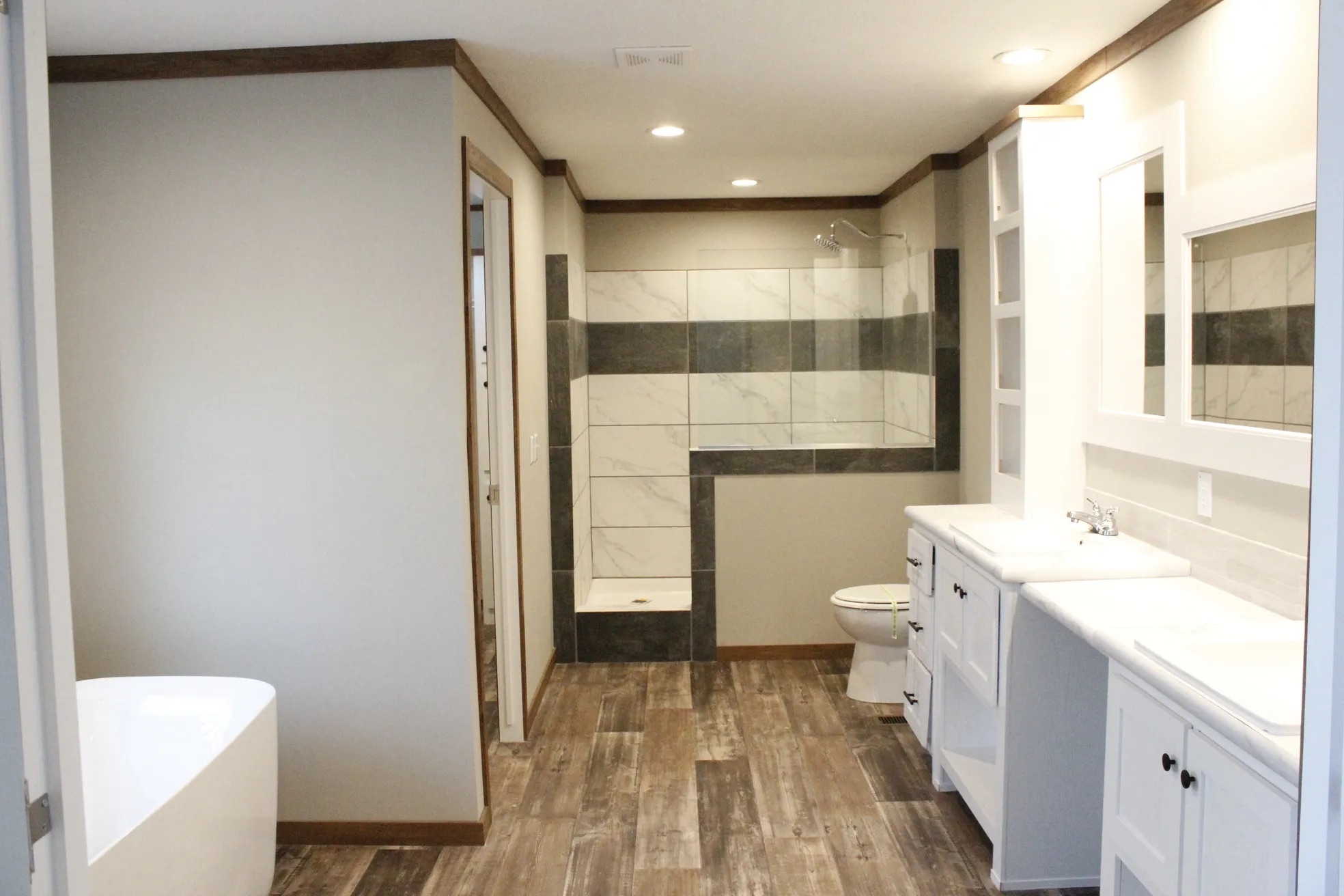 Spacious bathroom with wood-like floor tiles, a freestanding bathtub, modern glass shower, and dual-sink white vanity, creating a sleek, serene ambiance.