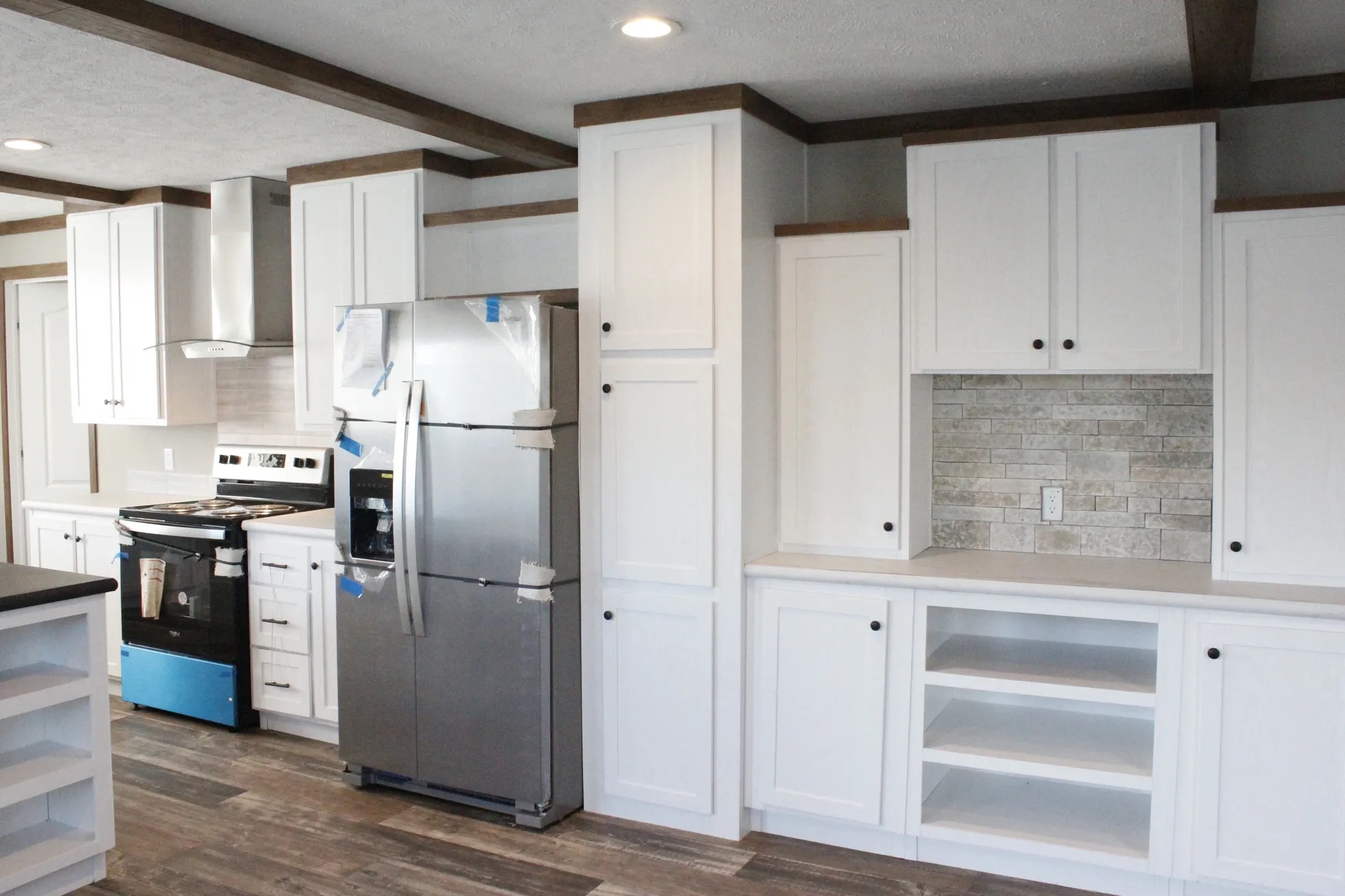 Modern kitchen with white cabinets, stainless steel fridge, and a stove. Brick backsplash adds texture. Wood flooring creates a warm tone.