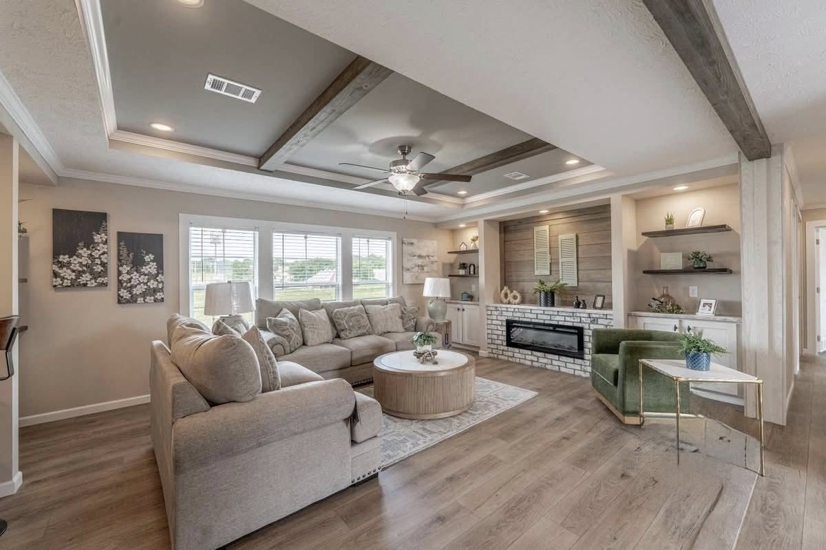 Cozy living room with sectional sofa, wooden coffee table, and modern decor. Large windows, recessed ceiling with fan, warm lighting, and hardwood floor.