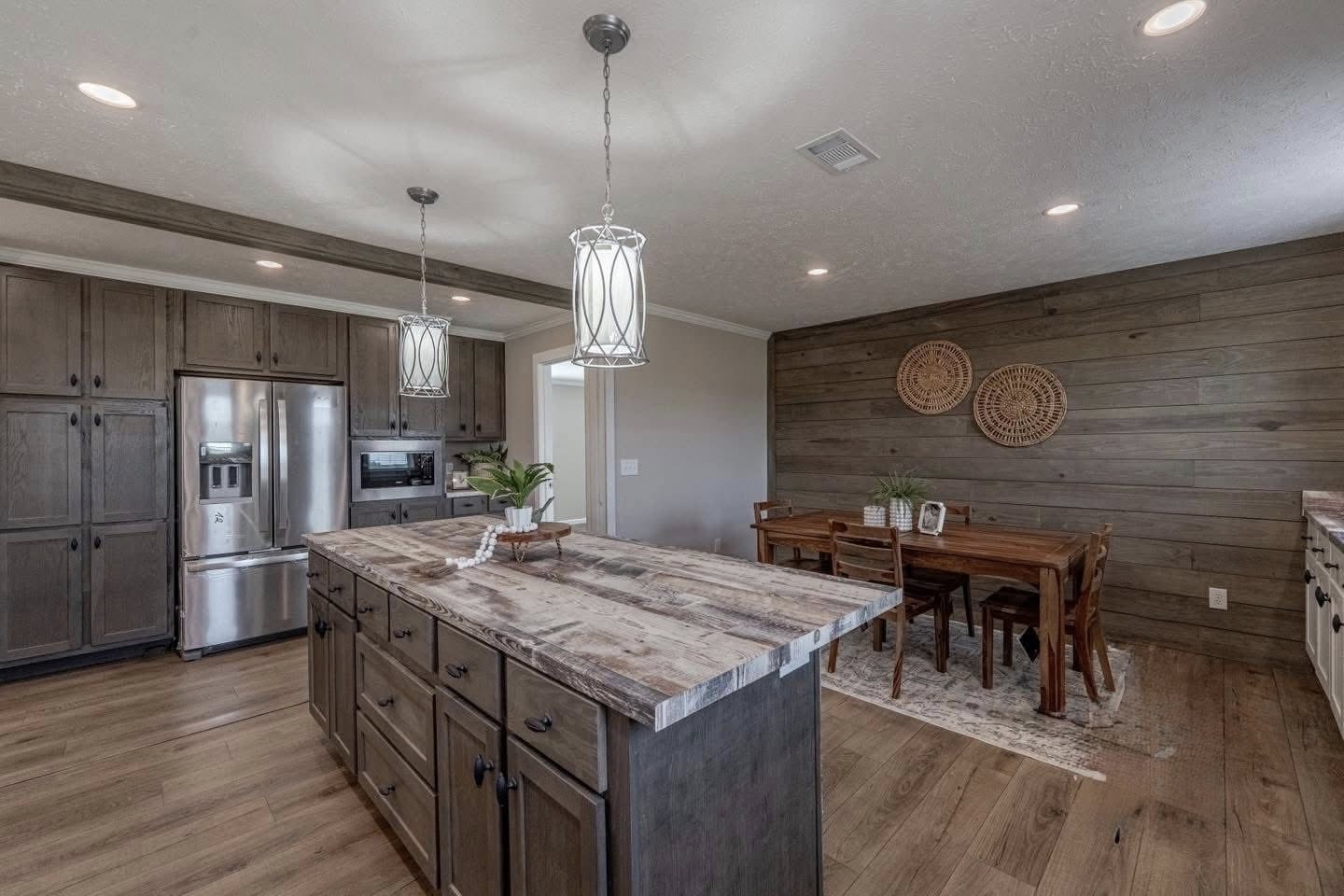 Spacious kitchen with rustic wooden floors, an island with pendant lights, and a dining area. Features wooden cabinetry and modern stainless steel appliances. A cozy, inviting atmosphere.