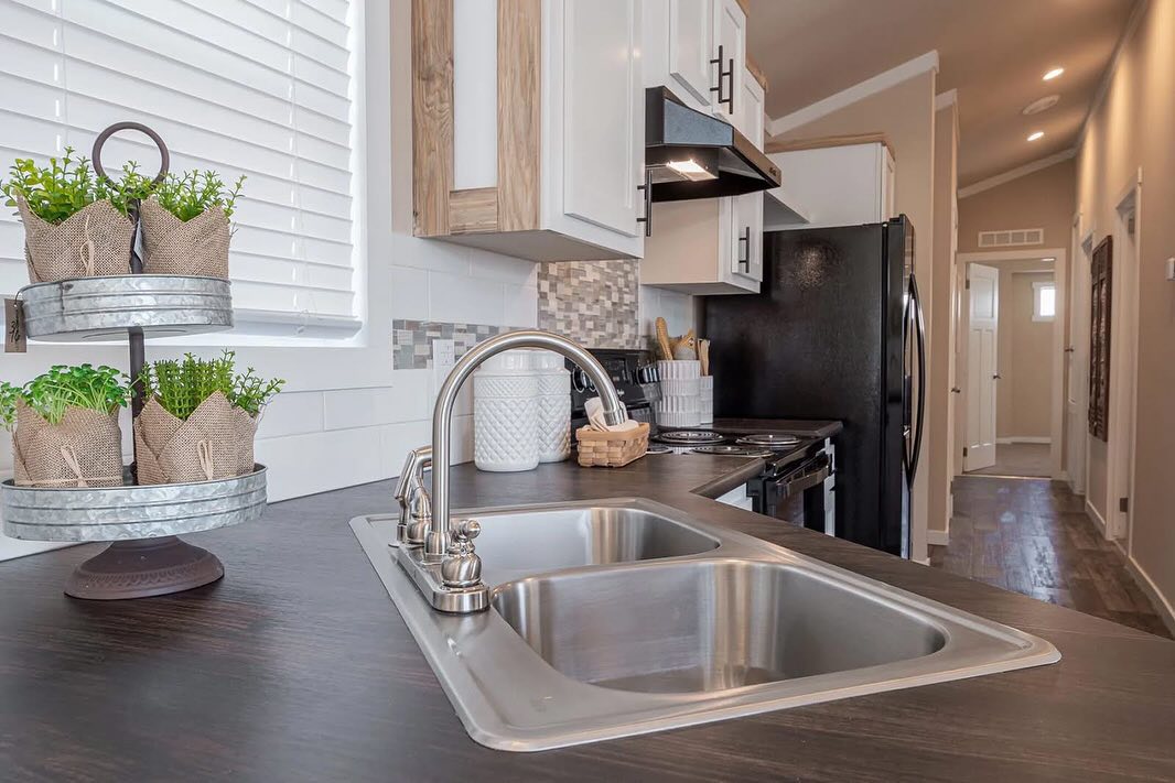 Modern kitchen with a sleek sink, dark countertop, and white cabinets. Herb planters and kitchenware add a cozy, inviting touch.