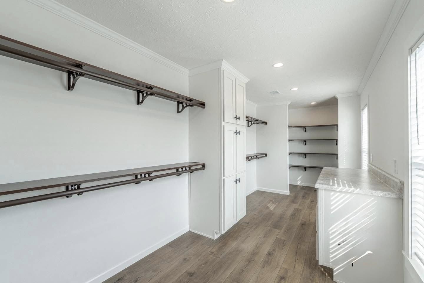 Spacious pantry with wooden shelves on white walls, white cabinets, and a marble countertop. The light wooden floor adds warmth to the bright space.