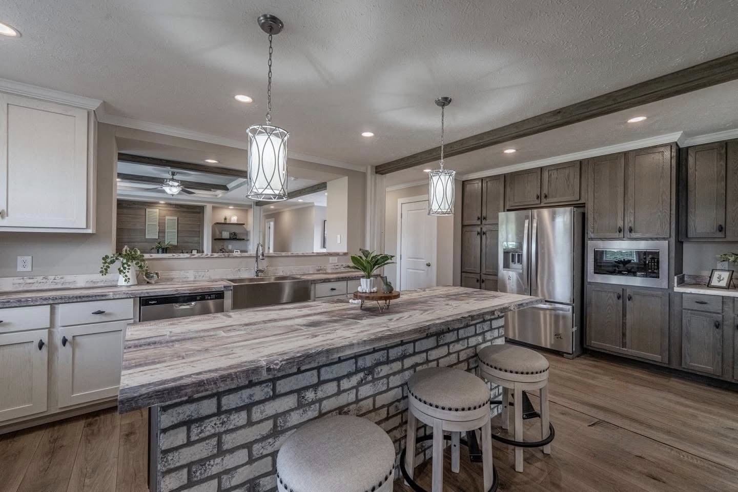 Spacious kitchen with rustic charm, featuring a brick island with light wood countertop, three cushioned stools, stainless steel appliances, and pendant lights.