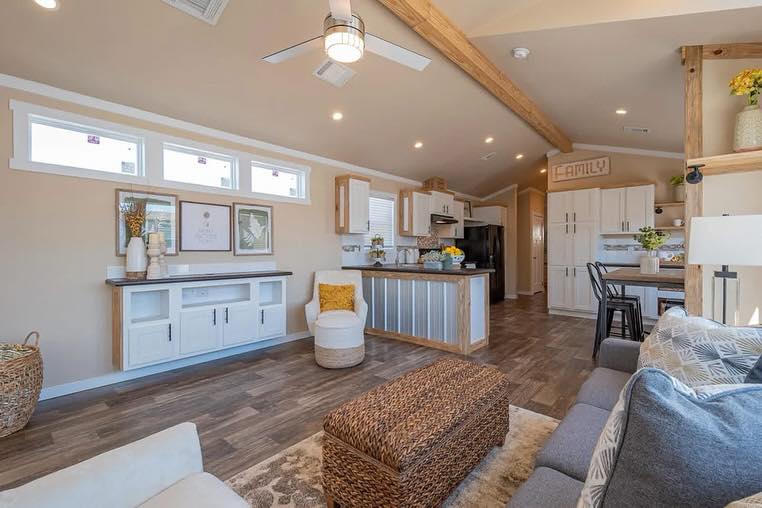 Cozy living room with modern farmhouse decor. Light walls, wood floors, woven ottoman, and a kitchen island create a warm, inviting atmosphere.