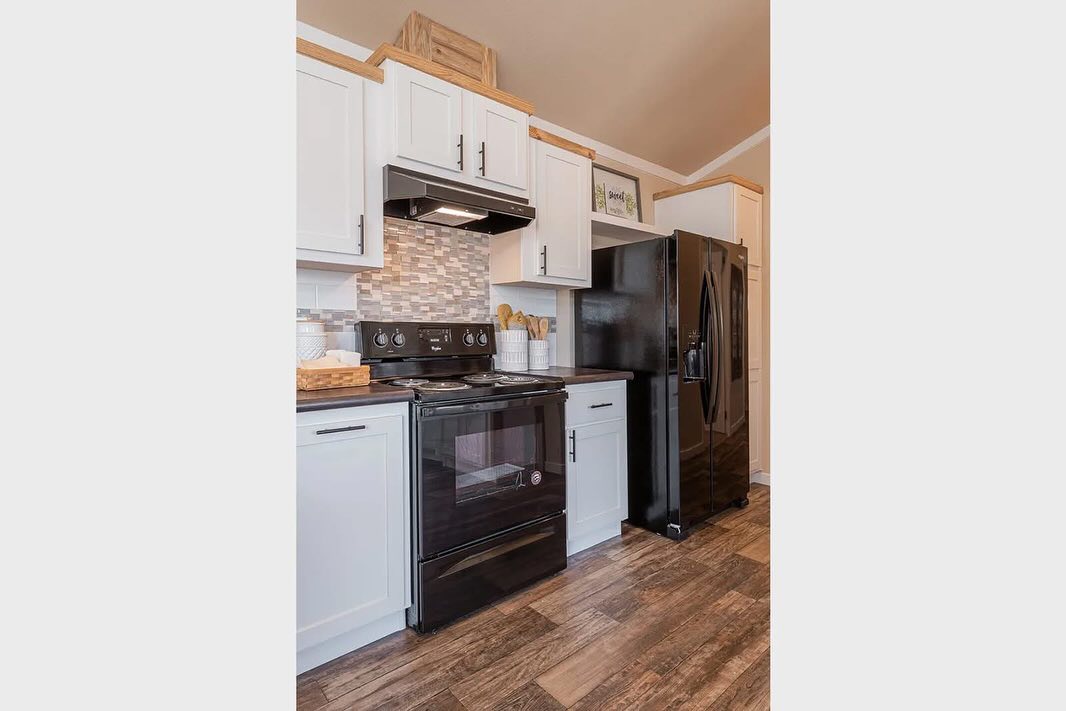 Modern kitchen with white cabinets, black appliances, and a tiled backsplash. Wooden accents and utensils add warmth to the space.